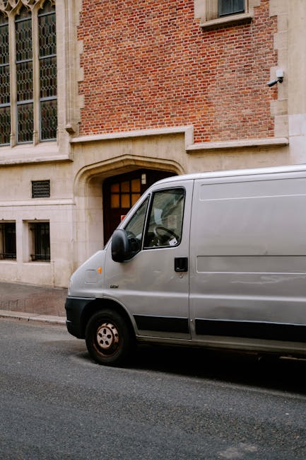 Inside the rear of a white van, numerous moving boxes of various sizes are stacked, some with visible 'Fragile' labels and handling instructions, indicating careful packing for a home relocation. The